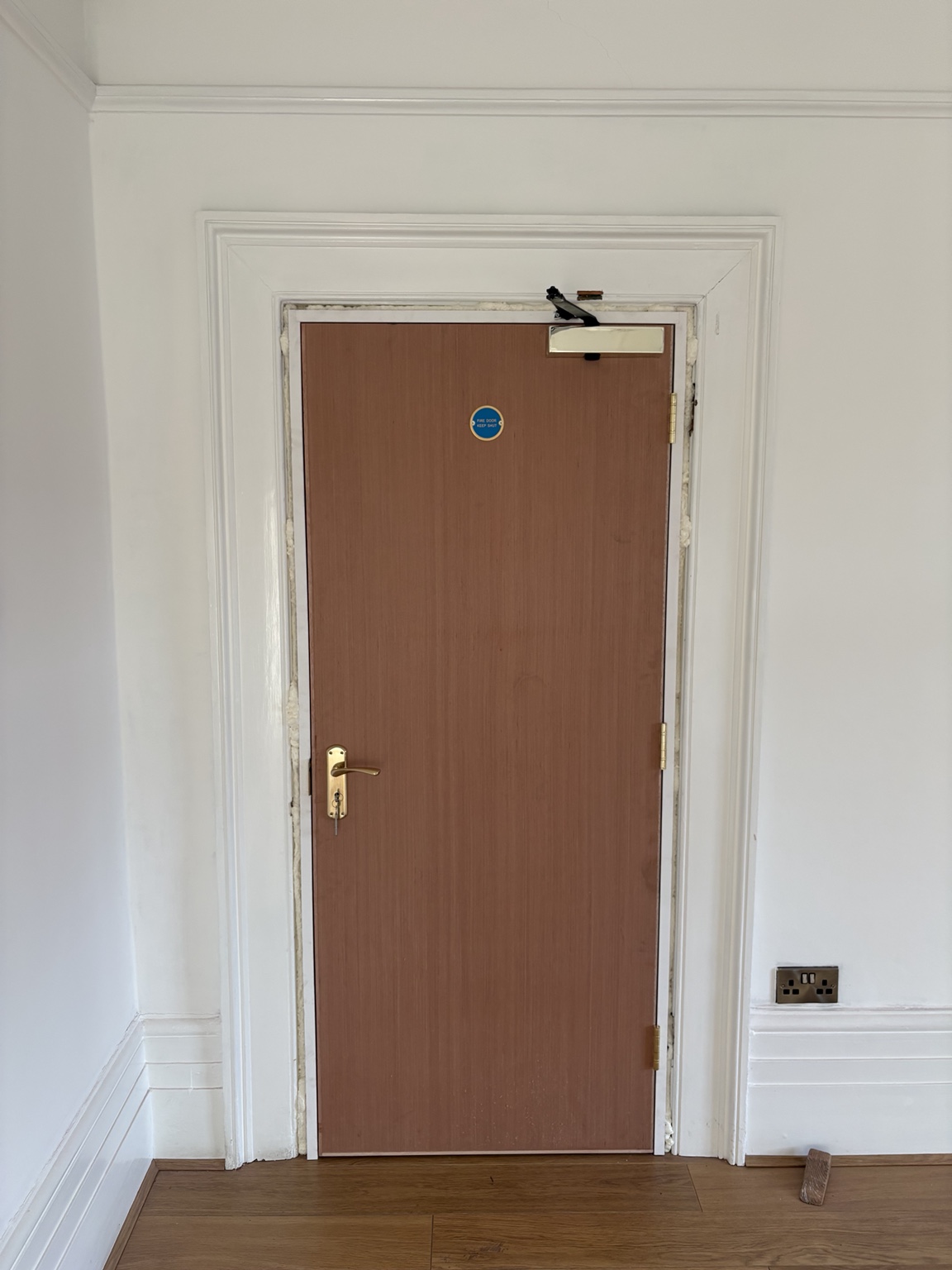 Newly fitted fire door with glazed vision panel, closer and fire exit signage during installation, with surrounding making good still incomplete